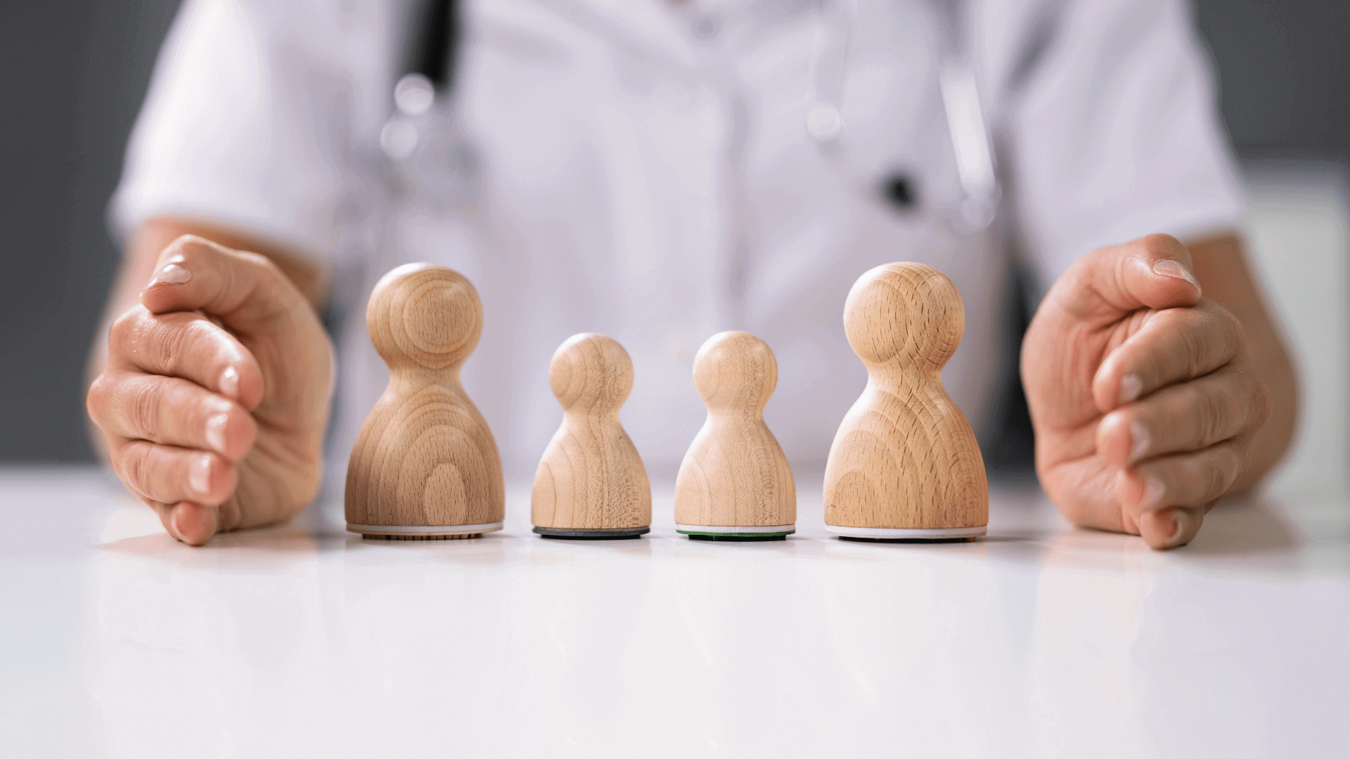 Vier Holzfiguren in unterschiedlichen Größen auf einem Tisch, gehalten von einer Person mit weißen Handschuhen.